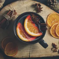Kubek grzańca z pomarańczą, cynamonem i anyżem na drewnianej desce.